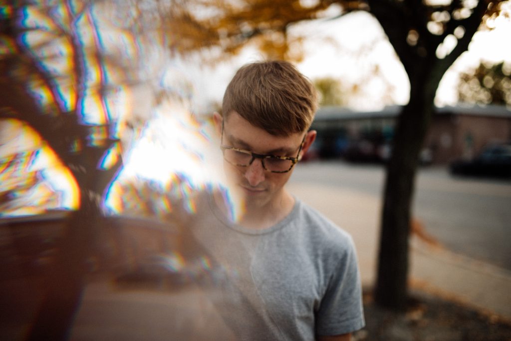 Handsome man looks at ground while prism reflects autumn trees into the frame.