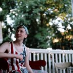 Boy in denim hat and American Flag tank talks to friend outside the frame.