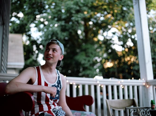 Boy in denim hat and American Flag tank talks to friend outside the frame.