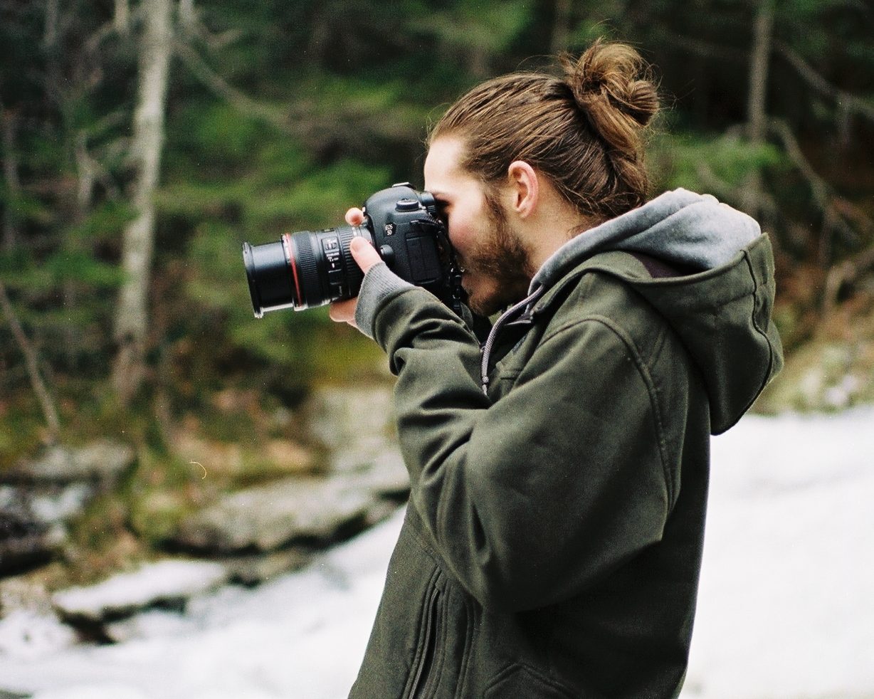 Man with hair in bun looks through viewfinder.