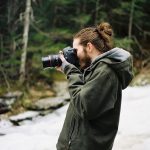 Man with hair in bun looks through viewfinder.