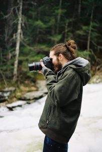 Man with hair in bun looks through viewfinder.