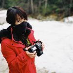 Girl in bright red coat reviews photos on the back of her DSLR.