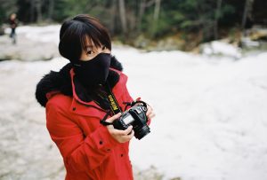 Girl in bright red coat reviews photos on the back of her DSLR.