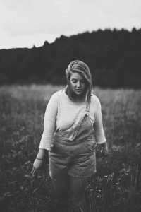 Girl in overalls walks through field, feeling the grasses and flowers.