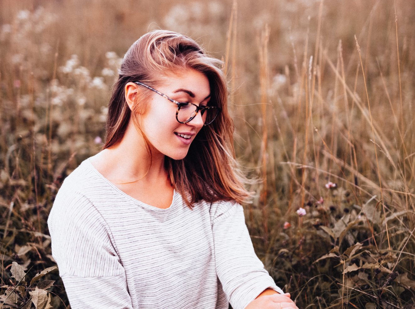 trendy girl sits in field of autumn grasses.