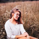 trendy girl sits in field of autumn grasses.