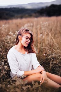 trendy girl sits in field of autumn grasses.