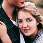 Cute couple embraces on a mountain. Girl looks directly into camera with passion in her eyes and smile.