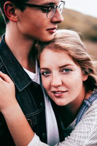 Cute couple embraces on a mountain. Girl looks directly into camera with passion in her eyes and smile.