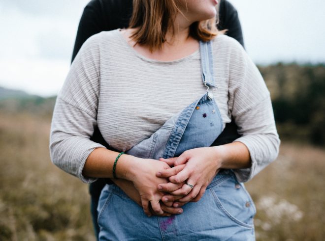 Couple holds hands and looks off into the distance. A ring is visible on the girl's finger.