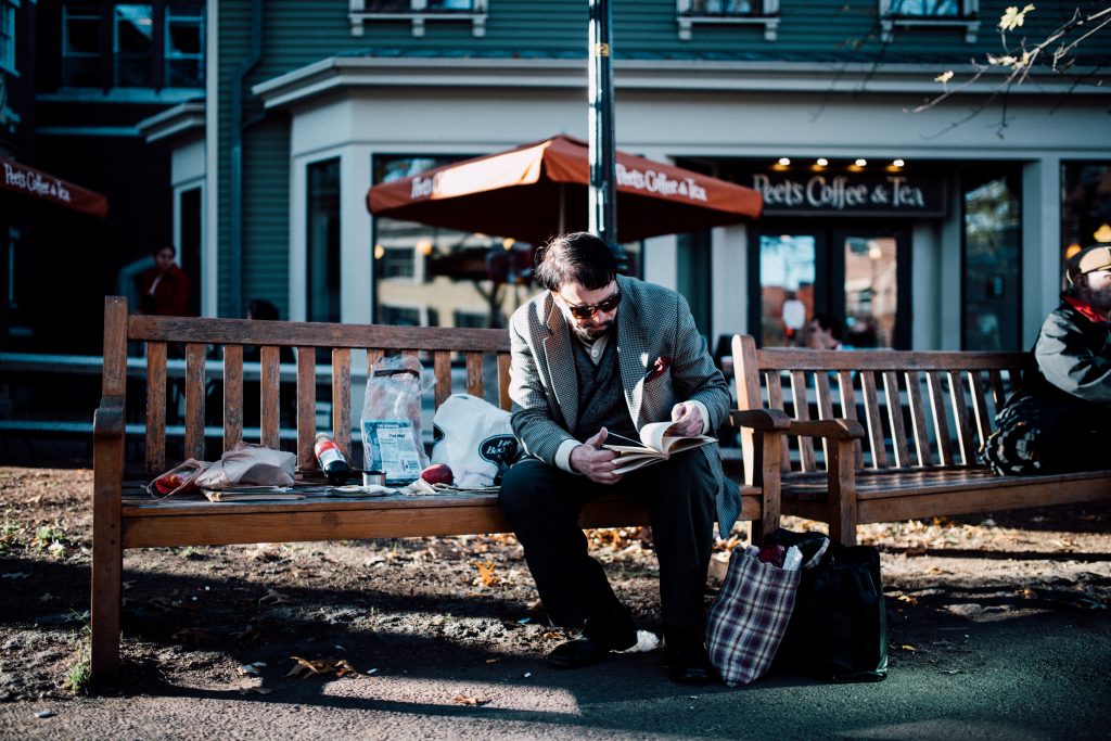 Elderly gentlemen reads a book and spreads out his belongings outside the Peet's Coffee in Harvard Square