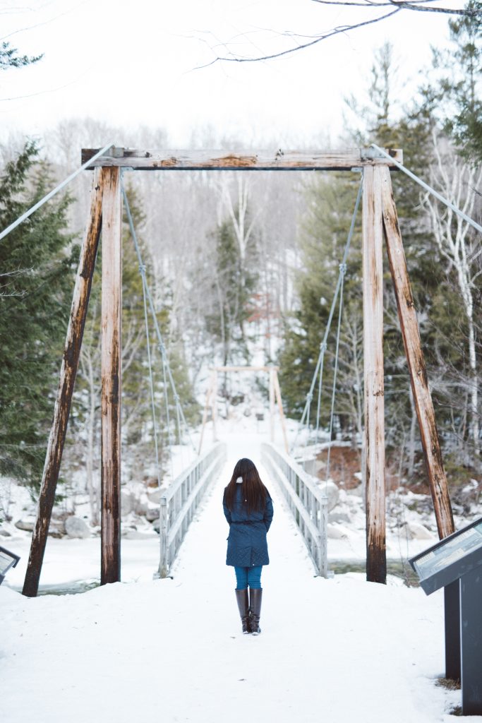 Girl in blue winter coat stands at the end of a robust bridge.