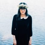 Woman in a floral crown sheepishly smiles for a centered portrait.