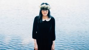 Woman in a floral crown sheepishly smiles for a centered portrait.