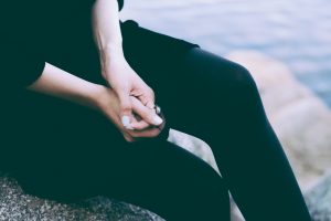 Torso of a woman mid-leg cross. Hands are folded and she is wearing a vintage ring.