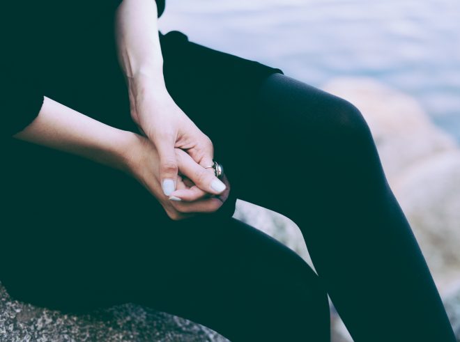 Torso of a woman mid-leg cross. Hands are folded and she is wearing a vintage ring.