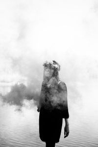 Danielle stands in front of a lake with smoke all around her.