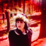 Wearing a flower crown, attention is drawn to Danielle by a deep red vignette.